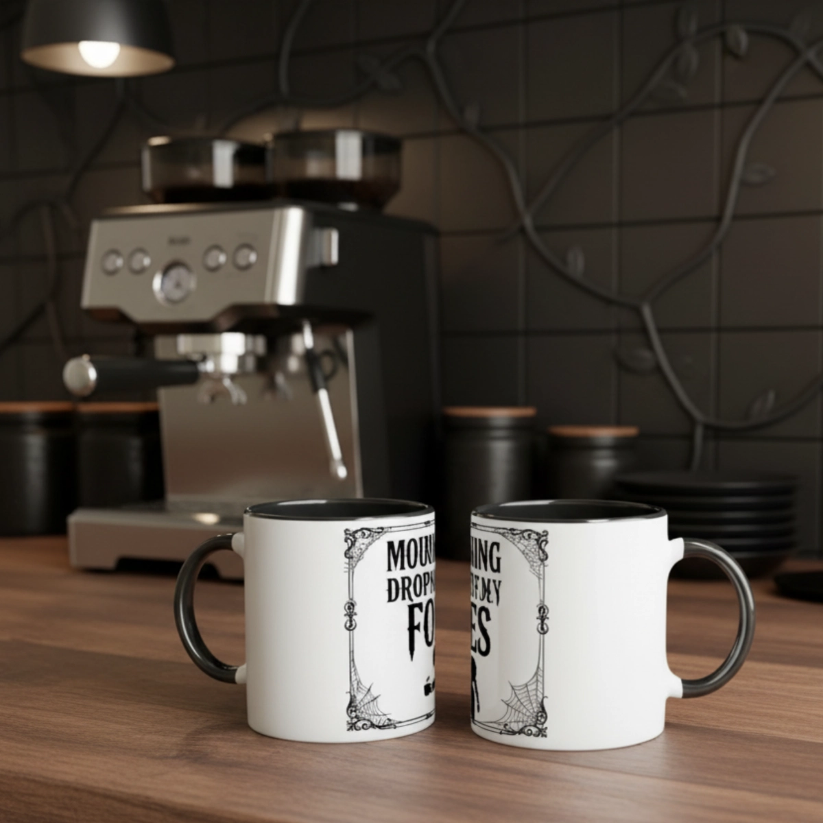 Two white ceramic mugs with black handles featuring the Mourning Drops design on a coffee counter near an espresso machine.