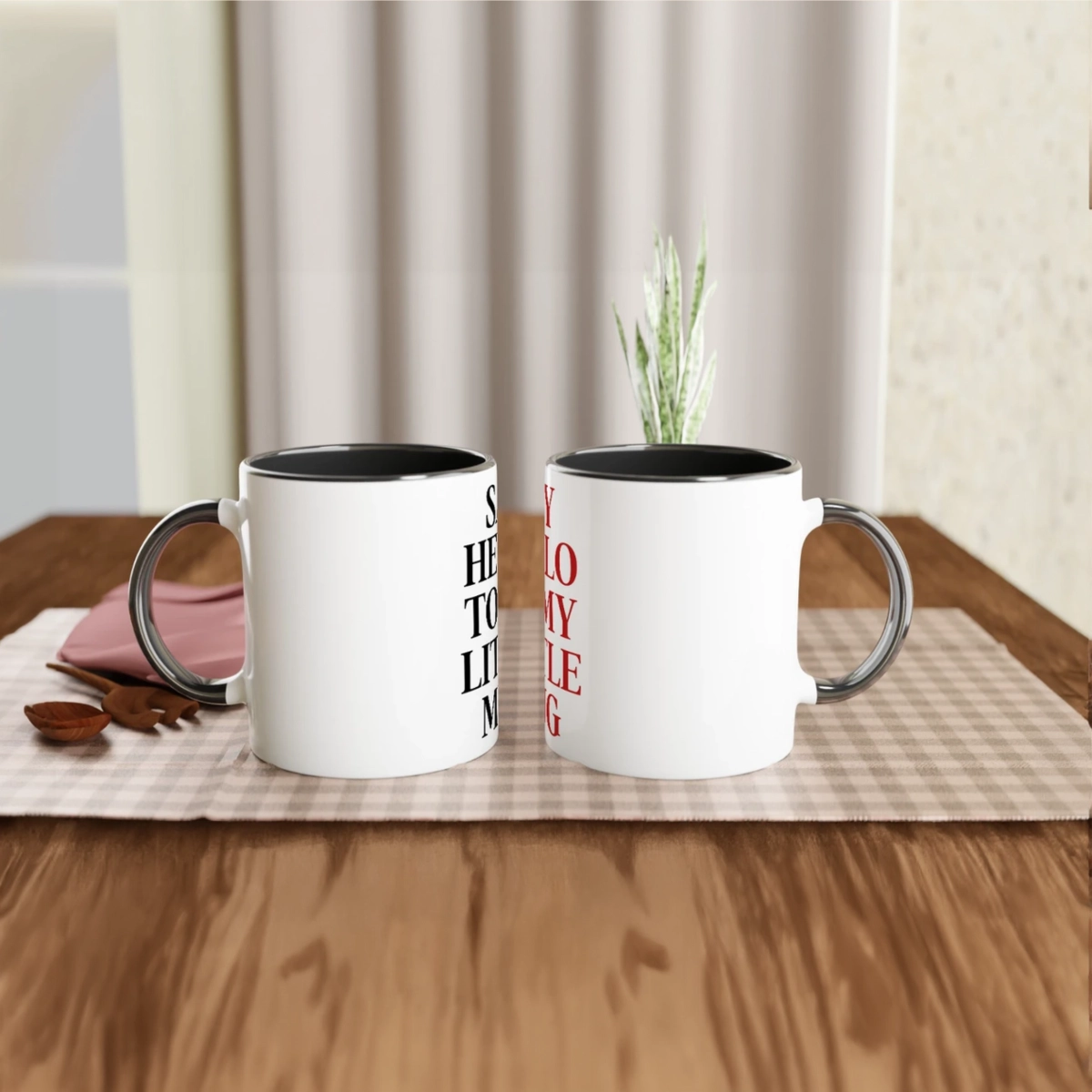 Two white ceramic mugs with black handles and black interiors featuring the Say Hello To My Little Mug text design on a table.
