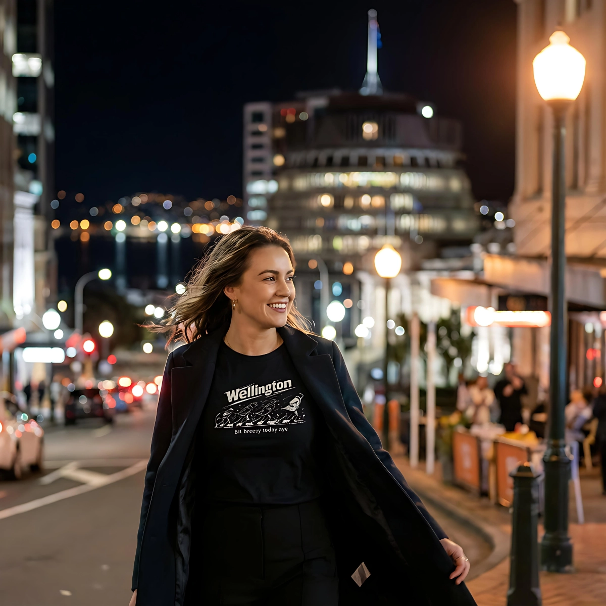 Person wearing a black Wellington Breezy T-shirt on a city street at night.