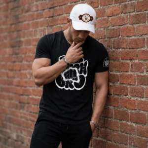 Model wearing a black Too Much Bro graphic T-shirt and white cap.