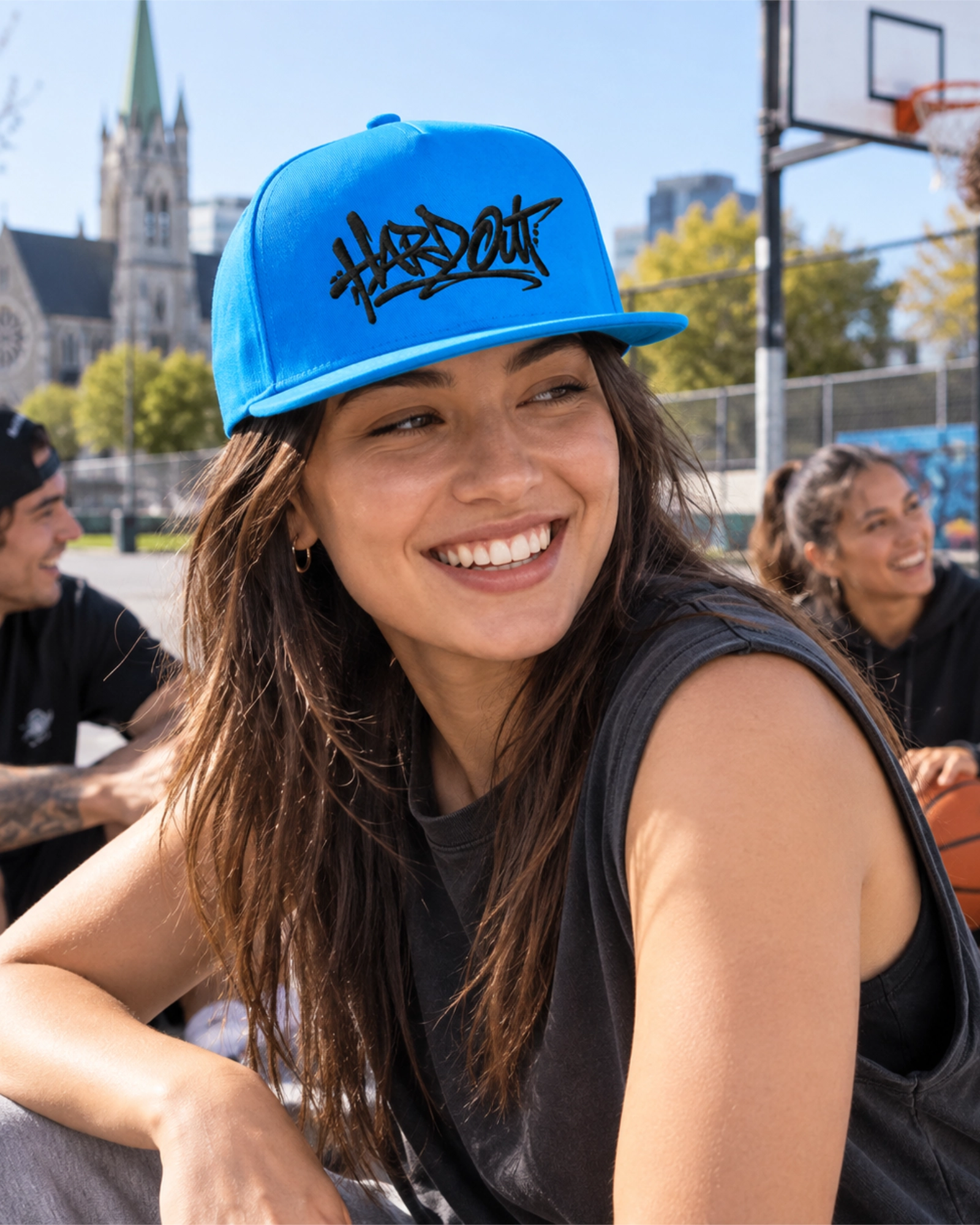 Woman wearing a blue HARDOUT flat bill cap with black embroidery at an outdoor basketball court