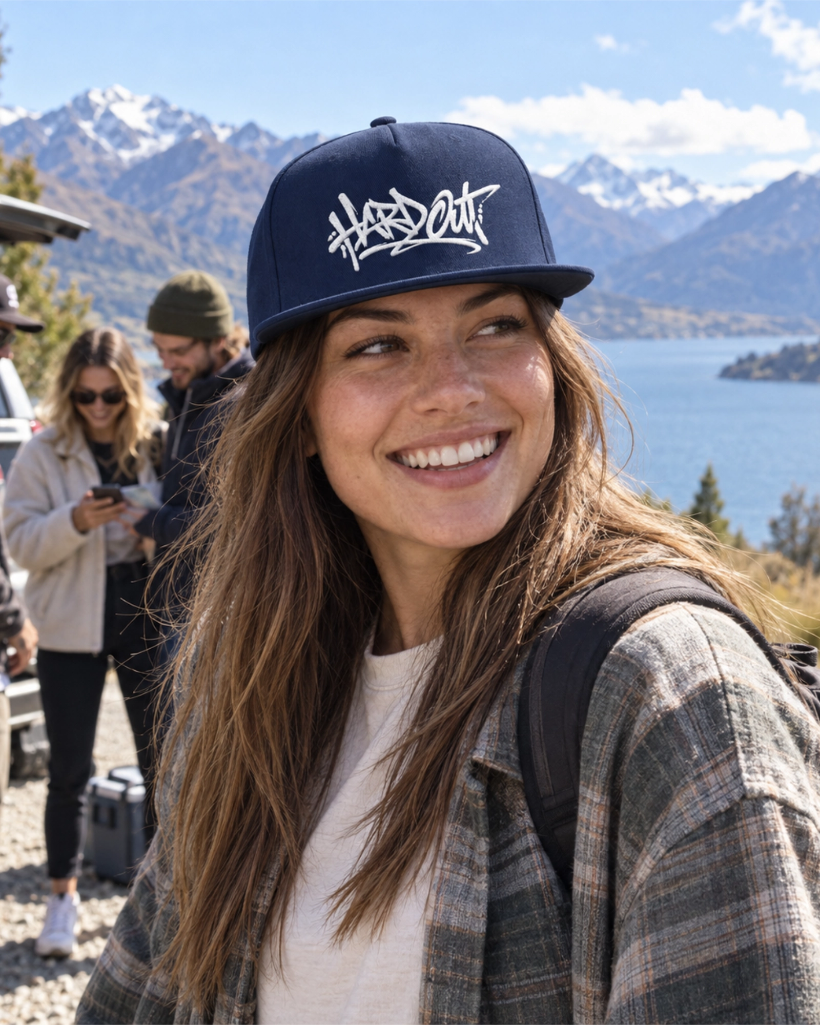 Woman wearing a navy HARDOUT flat bill snapback cap with white embroidery on a South Island road trip