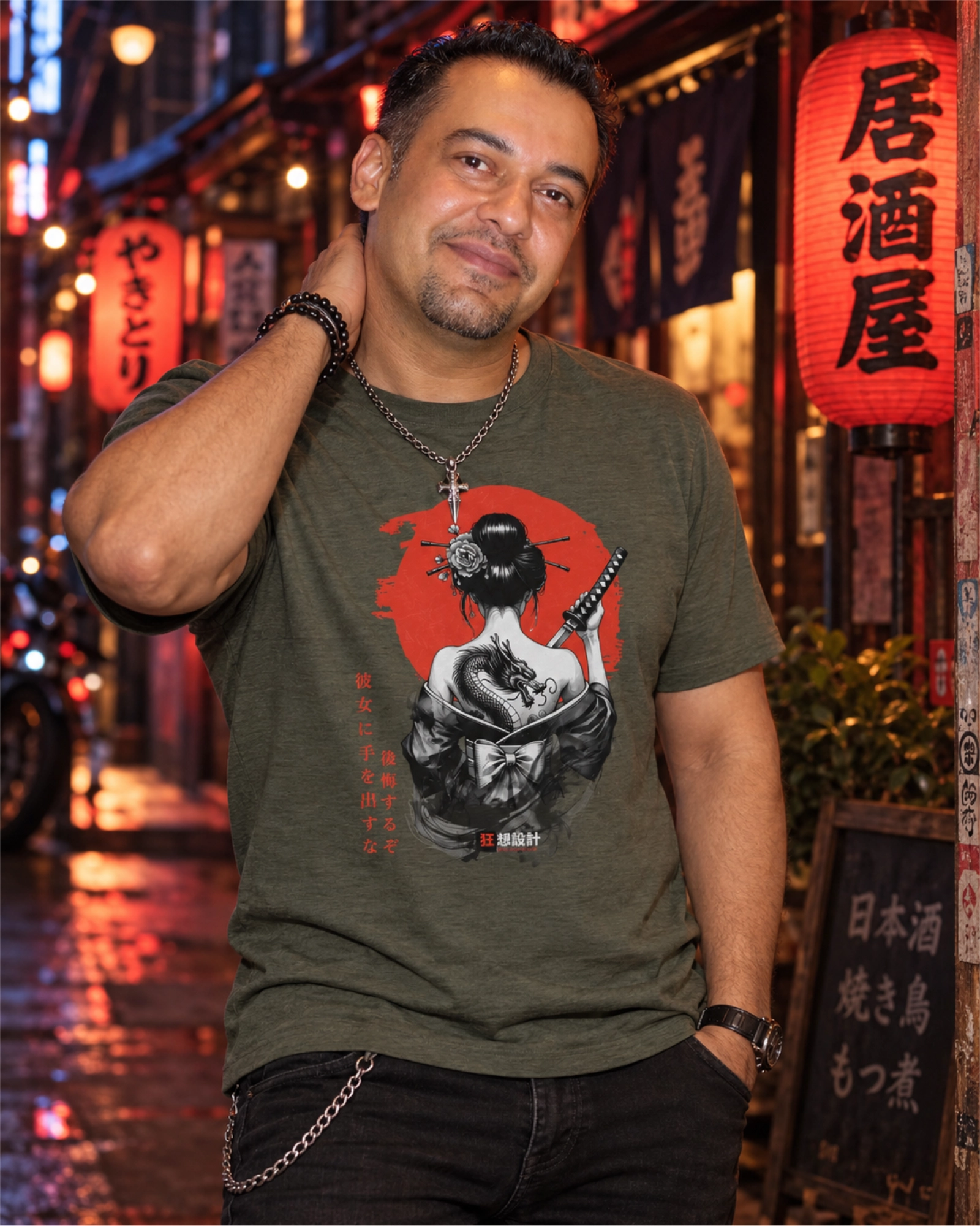Man wearing an olive-green Onna-Bugeisha graphic T-shirt featuring a woman with a dragon tattoo and katana, on a lantern-lit street at night.